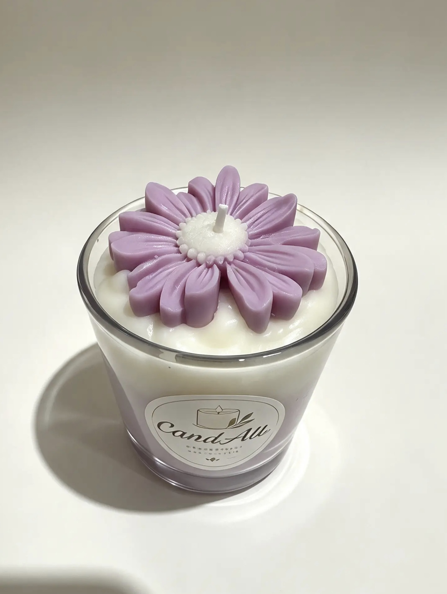 Candela in vetro con cera chiara e un grande fiore lilla in cera